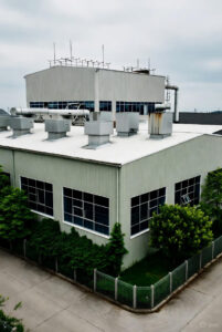 Moderne industribygning med metalventilation på taget, store vinduer og grønne buske omkring